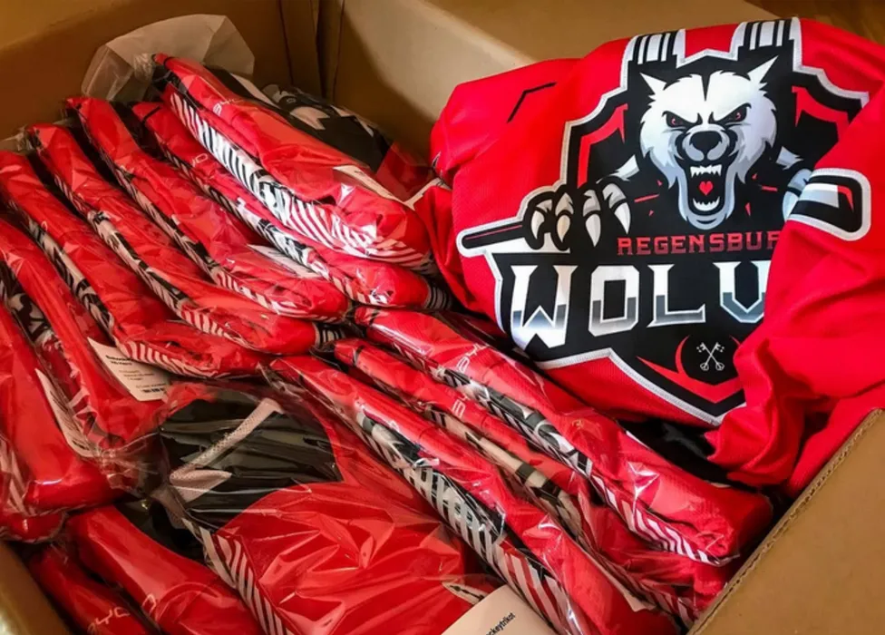 A box filled with red customized sports jerseys, including one with a wolf logo and the text 'Regensburg Wolves'.