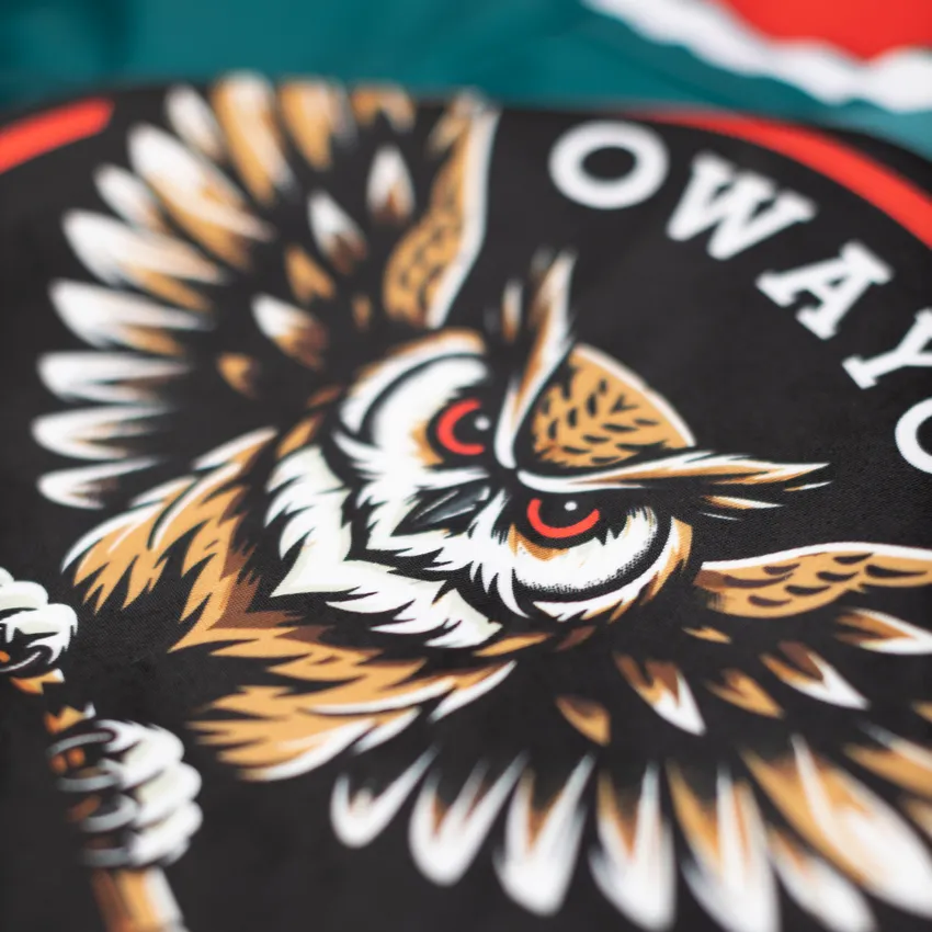 A detailed, colorful design of an owl motif on a black background, featured on a sportswear item from owayo.