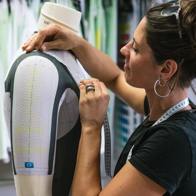 A woman adjusts a customized sportswear garment on a mannequin while wearing a measuring tape.