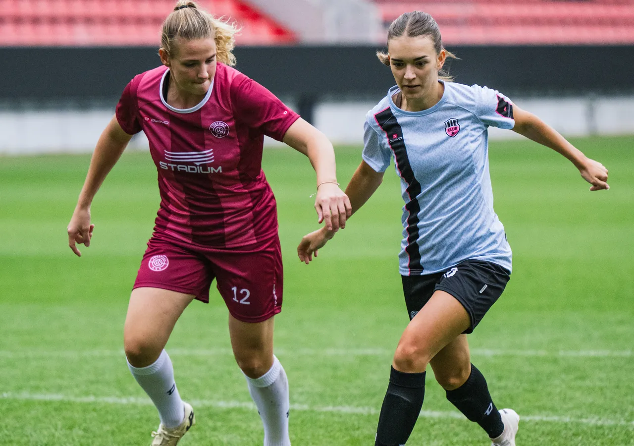 Two women in sportswear are playing soccer on a grass field.