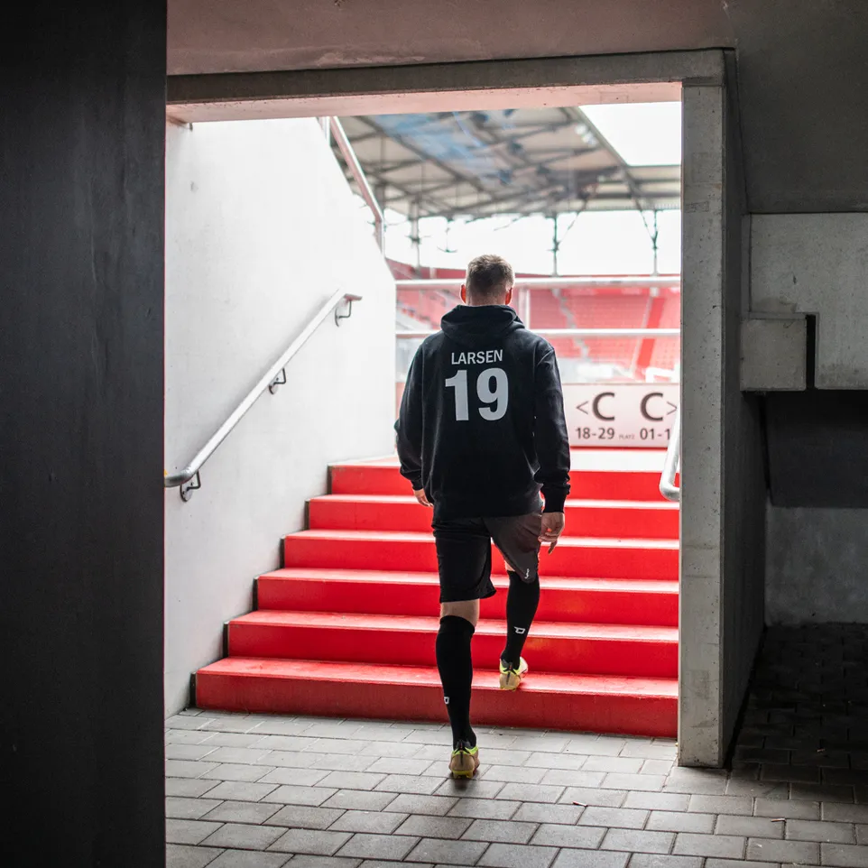 An athlete wearing a black hoodie and shorts is walking up a red staircase in a stadium.