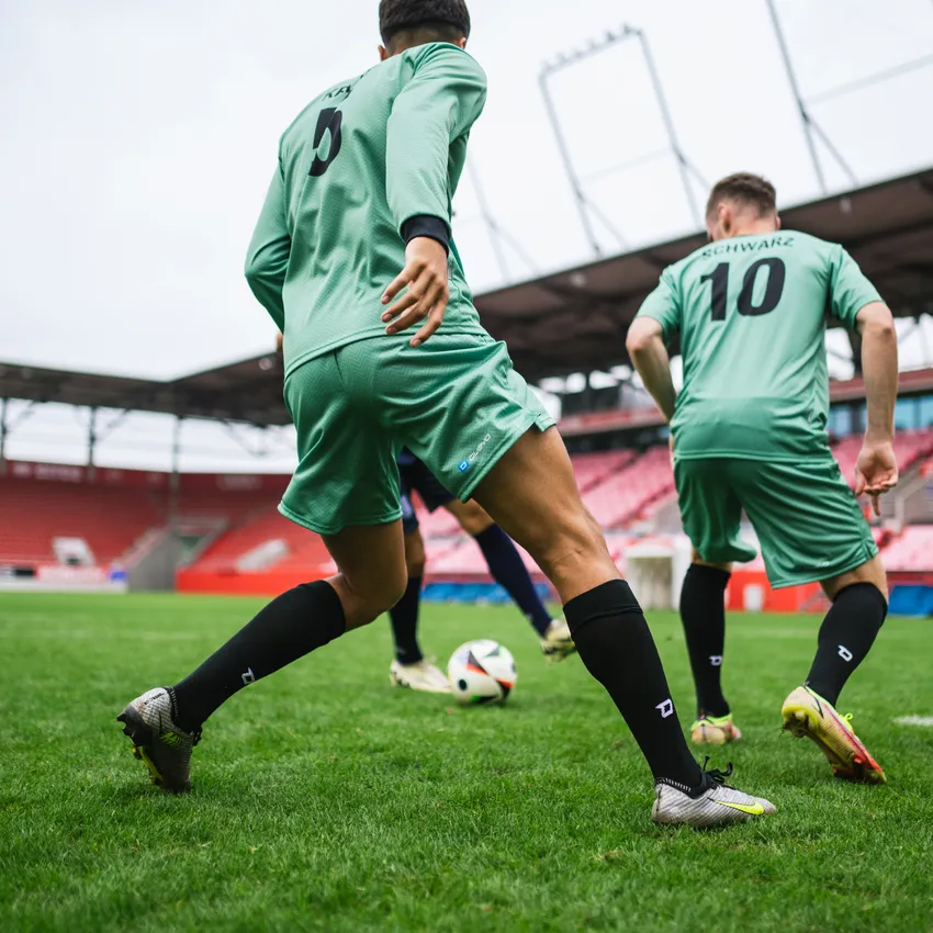 Two players in green soccer jerseys and black socks playing on a field in a stadium.