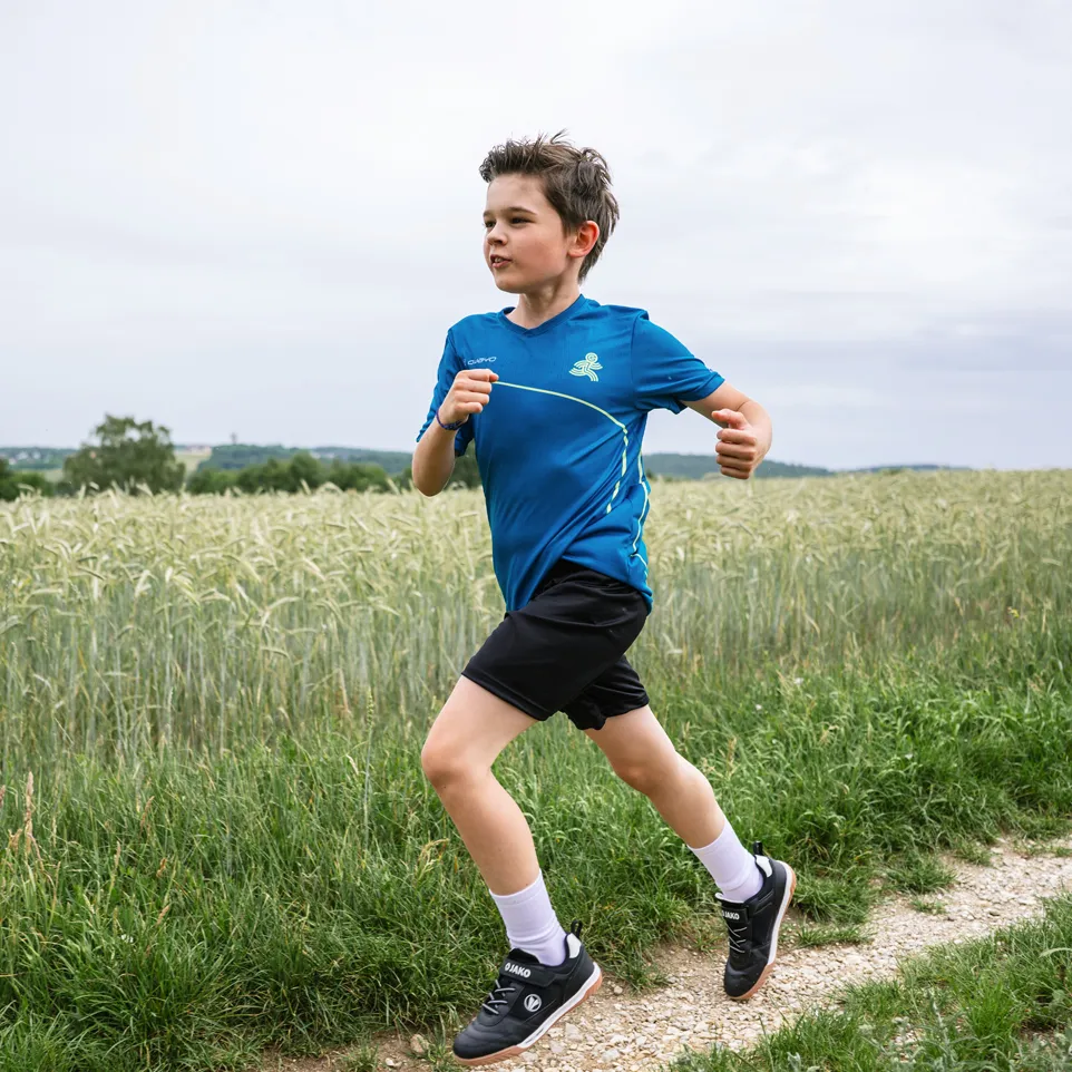 A boy is running on a dirt path, wearing a blue sports shirt and black shorts.