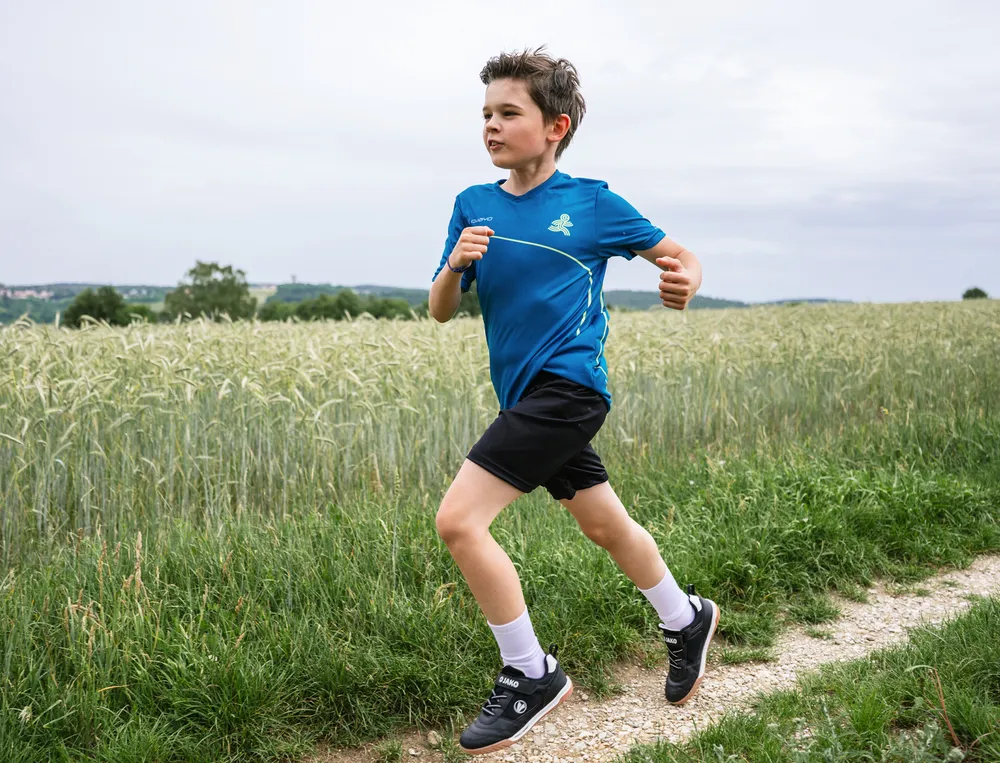 A boy is running on a dirt path, wearing a blue sports shirt and black shorts.
