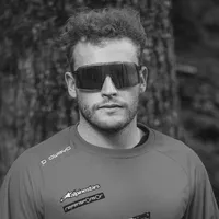 A man with curly hair and sunglasses wears a grey long-sleeved sport shirt with the 'owayo' logo on the shoulder and other sponsor logos on the chest.