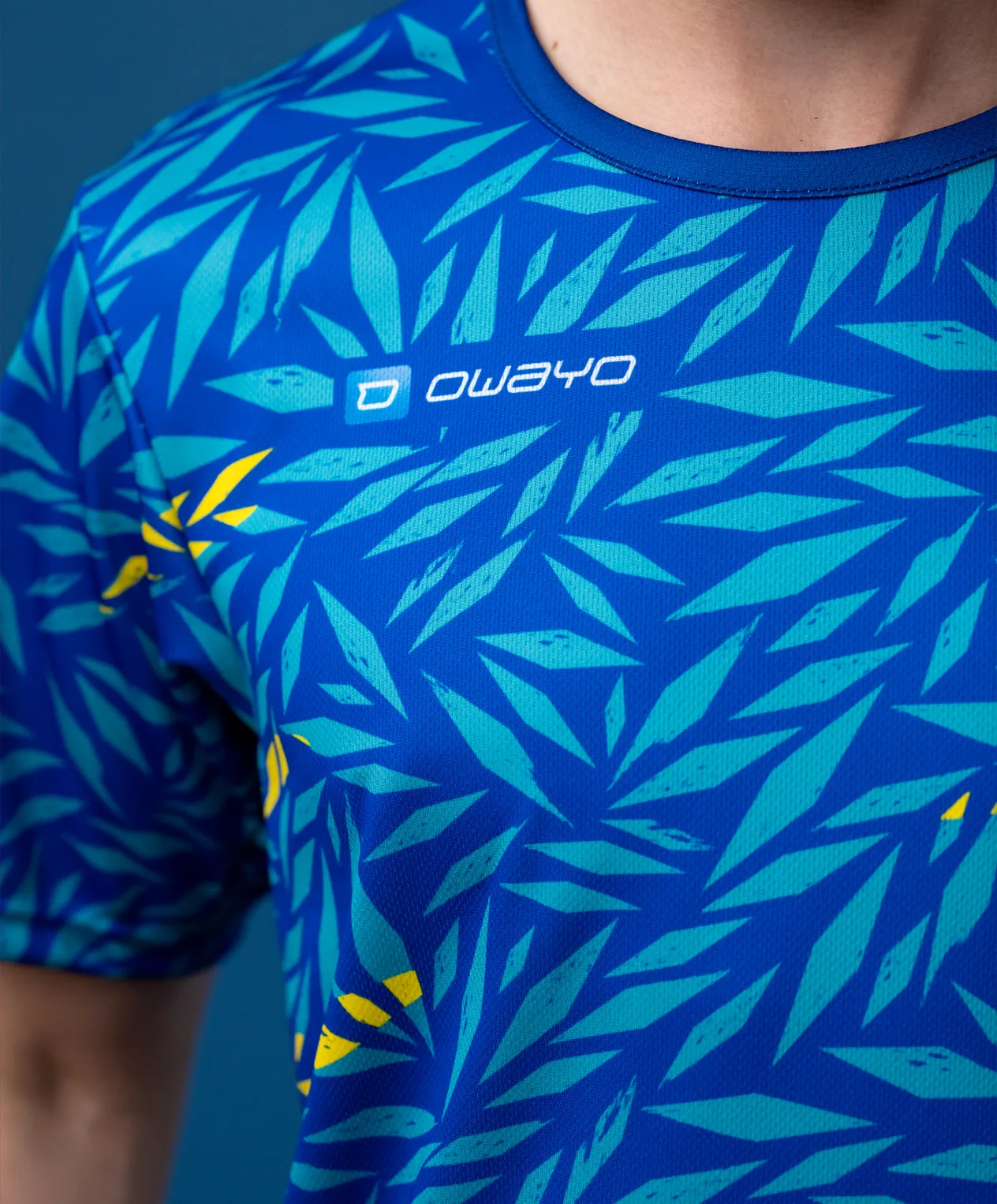 A sporty, short-sleeved shirt featuring a blue leaf-like pattern in various shades of green with yellow accents.