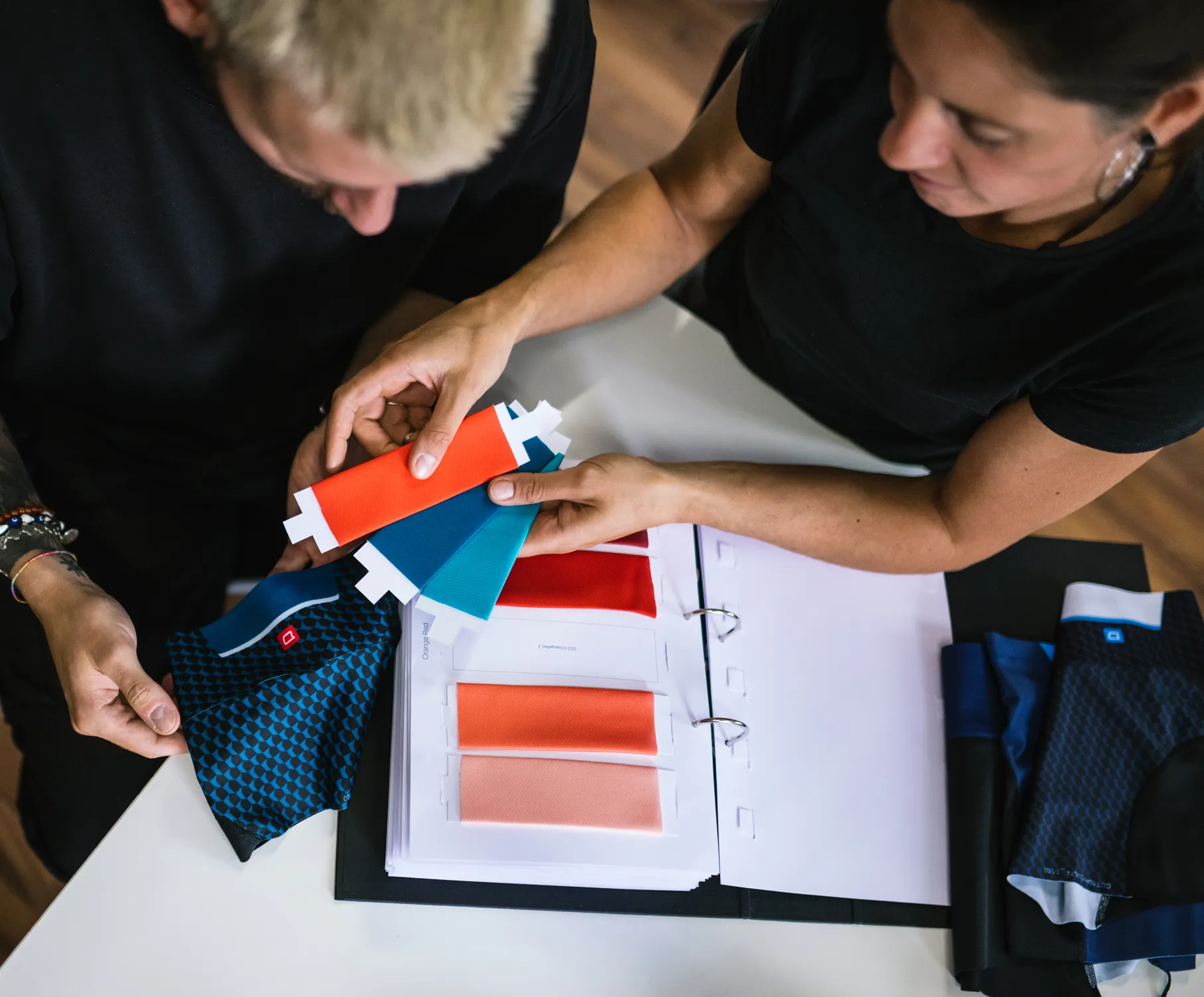 Two people select colors for customized sportswear by examining fabric swatches and a color chart.