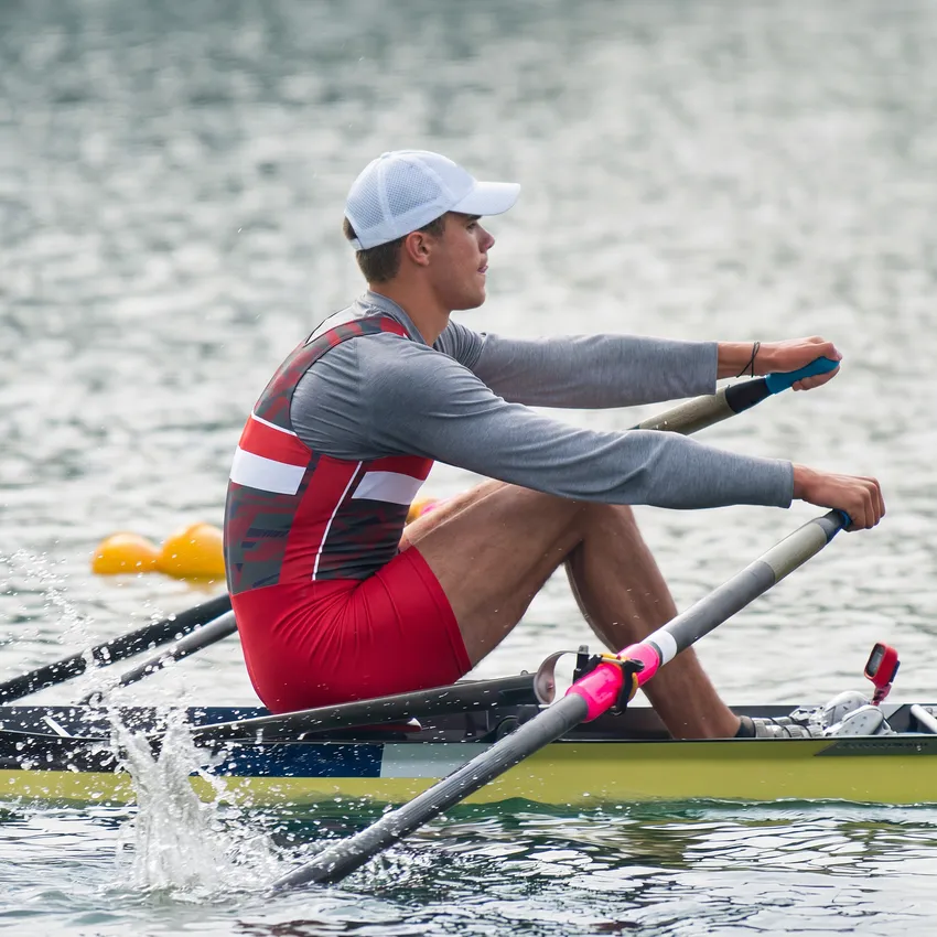 A rower in a red and gray sports outfit is rowing on a body of water.