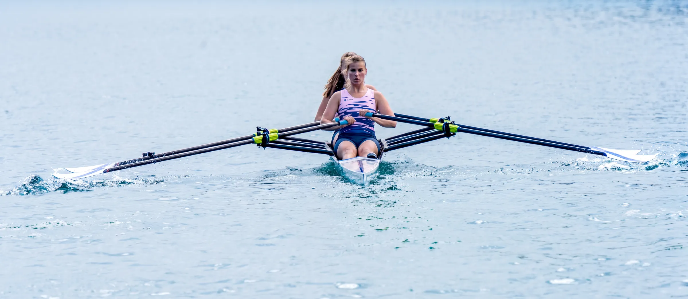 A rower is paddling in a single scull on calm water.