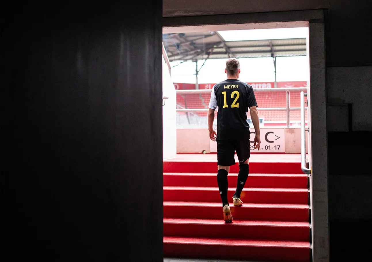 A soccer player wearing a jersey with the name Meyer and number 12 walks up a red staircase into a stadium.